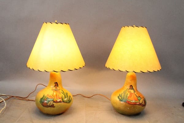 Two 14858. Pair Of Hand Painted Spanish Revival Monterey Period Lamps with gourd-shaped bases featuring pastoral scenes, lit and casting a warm glow on a neutral background.