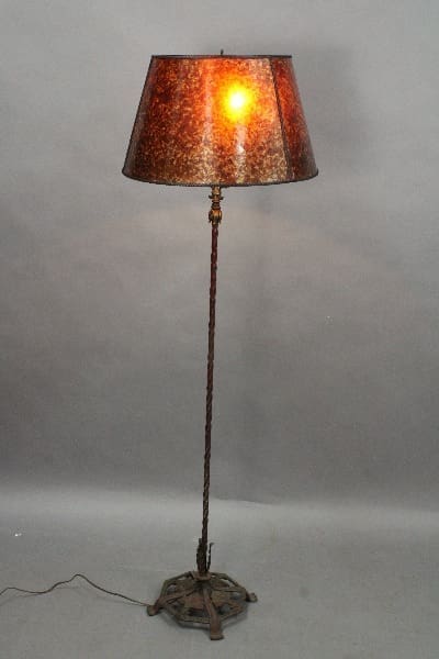 14868. Spanish Revival Floor Lamp With Polychrome Base with a rusted finish and an illuminated mottled shade, standing on a circular base, against a gray backdrop.