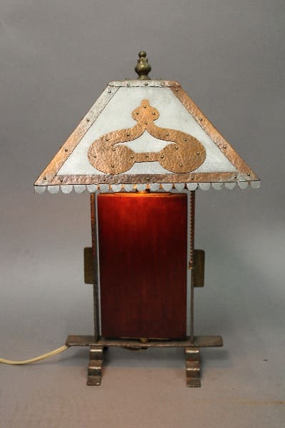 14874. Arts And Crafts Handmade Wood And Hammered Copper Lamp with a lit amber glass panel and a metal top featuring decorative cut-outs.