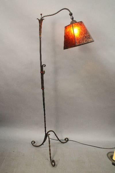 A 14924. Circa 1920's wrought iron floor lamp with a polychrome finish and a square, stained-glass shade, illuminated and standing on a plain background.