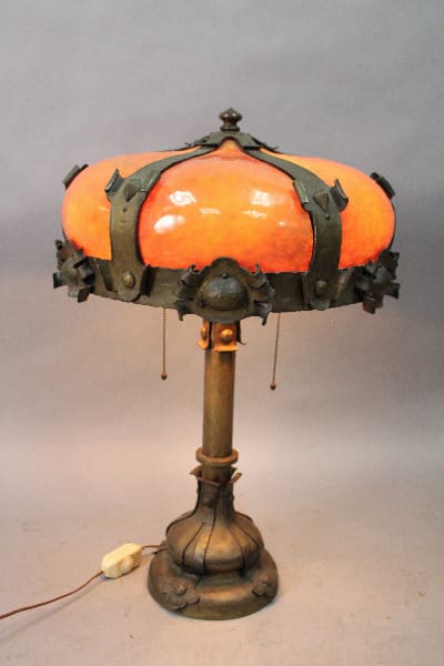 14986. Large Scale Arts And Crafts Art Glass Lamp with an orange glass shade and ornate metalwork, set against a grey background.