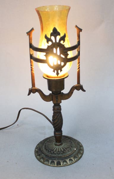 14997. Antique electric table lamp with ornate metal details, illuminated yellow glass shade, and a turned wooden base, on a white background.