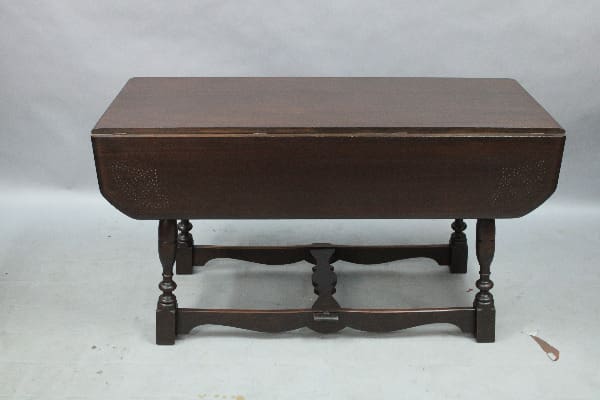 A 1920's Spanish Revival Folding Table with carved legs and a stretcher, closed and placed against a plain background.
