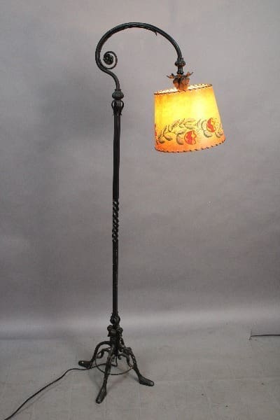 An 15036. Spanish Revival 1920's Iron Floor Lamp With Custom Shade with a curved metal pole and a colorful shade illuminated, against a plain backdrop.