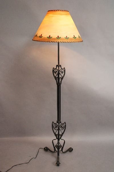An antique 15090's Wrought Iron floor lamp with ornate metalwork and a floral patterned lampshade, illuminated against a neutral background.
