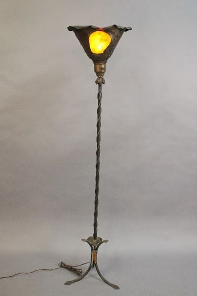 An 15128. 1920's floor lamp with a twisted metal stand, tripod base, and a glowing yellow glass shade, set against a neutral backdrop.