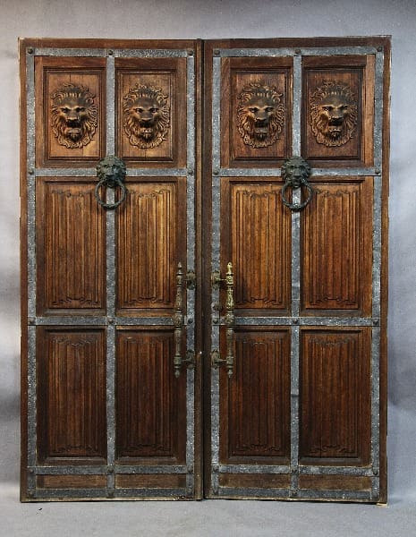 15346. Stately Turn Of the Century Pair of Palatial Doors With Linen Fold and Lion Carvings with metal ring knockers, set against a gray backdrop.