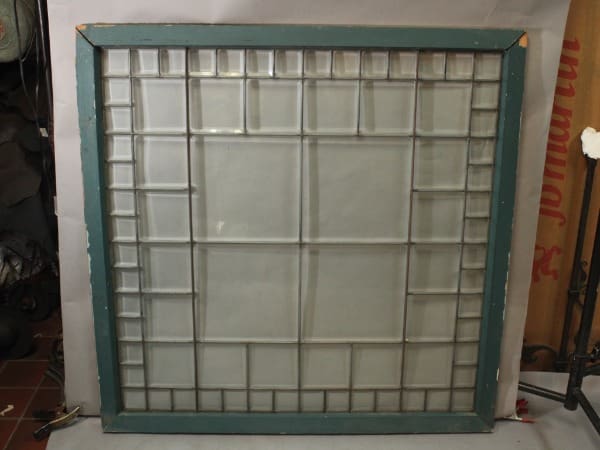 A vintage framed 15781. 1 of 2 Large Stained Glass Window with a worn green frame, sitting indoors against a cluttered background.