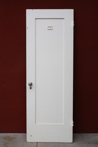 A 6551. 1920s Single Panel Interior Door CC with a silver handle, standing upright against a red wall.