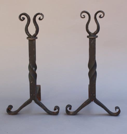 Sentence with product name: Two 7209. Pair Of Wrought Iron Andirons with spiral stems and curled top designs, standing on a plain background.
