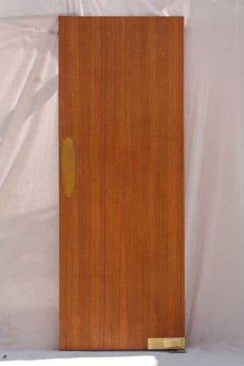 A vertical wooden door with a brass handle on the left side, standing against a draped white backdrop.