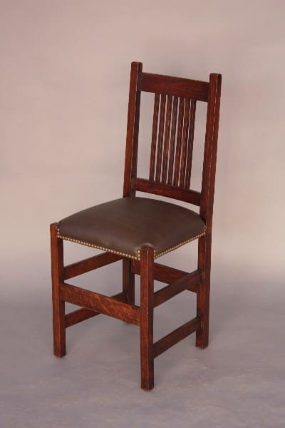 A 8632. Arts And Crafts Mission Chair with a vertical slat back and a brown leather cushion, accented with brass nailheads.