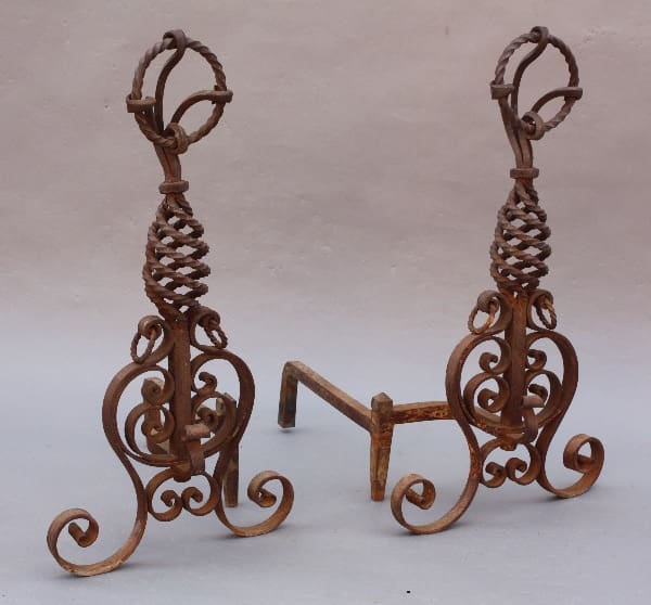 Two ornate 8741. 1920's Wrought Iron Andirons with spiral designs and curved accents on a light, plain background.