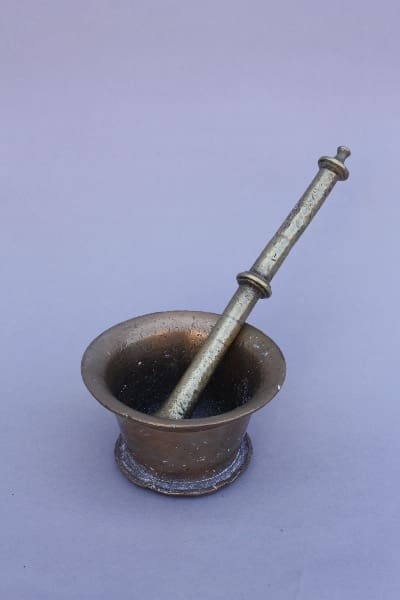 A small, 8798. 19th Century Solid Brass Mortar and Pestle with a pestle resting inside, against a plain light purple background.