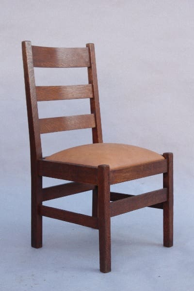 A 9804. 1910 Ladder Back Arts & Crafts Side Chair with three horizontal slats on the back and a cushioned seat, set against a plain gray background.