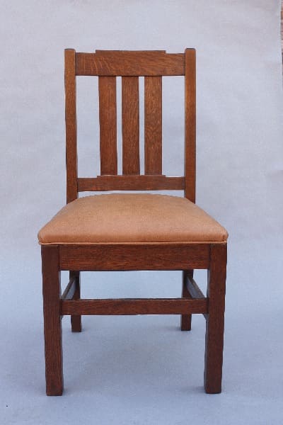 A 9806. 1910 Arts & Crafts Oak Side Chair with a vertical slat back and a beige upholstered seat cushion, set against a plain, light background.