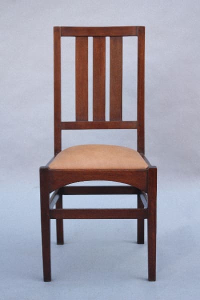 A 9807. 1910 Arts & Crafts Side Chair featuring a tall, vertical slat back design and a light beige cushioned seat, set against a plain gray background.