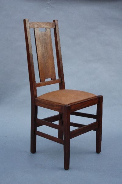 A 9817. 1910 Signed Gustave Stickley side chair with a vertical slatted back and a padded seat, standing on a grey background.