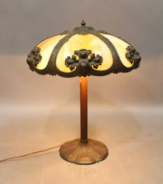 Turn Of The Century Table Lamp With Art Glass And Bronze Base featuring orange and cream panels accented with black decorative elements, on a wooden base.