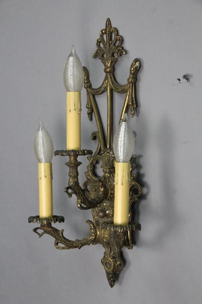 Three-armed brass wall sconce with candles.