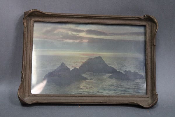 Framed artwork of rocky coastline at sunset.