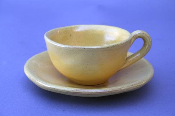 Yellow ceramic cup and saucer on purple background.