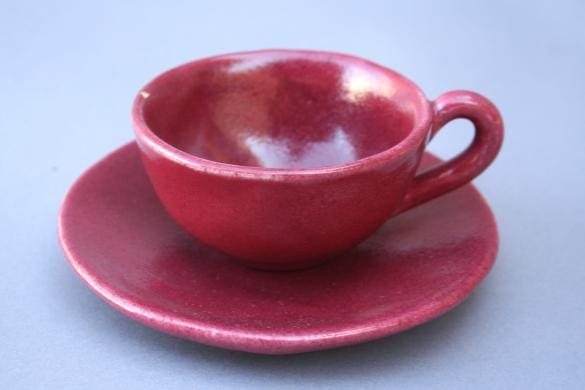 Red ceramic cup and saucer on gray background.