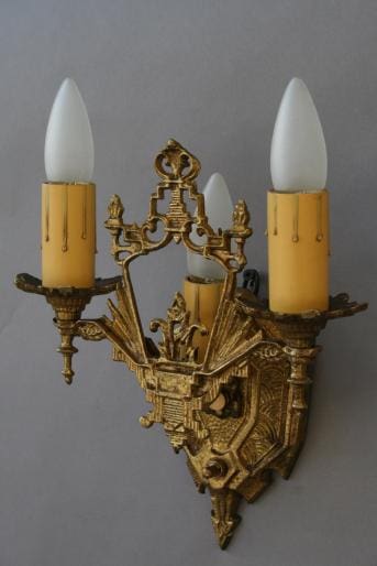 Ornate metal sconce with three candle lights.