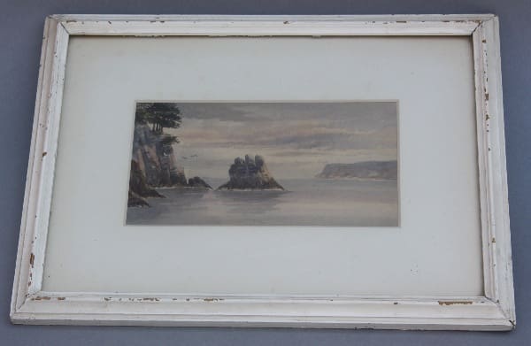 Coastal landscape painting in white frame.