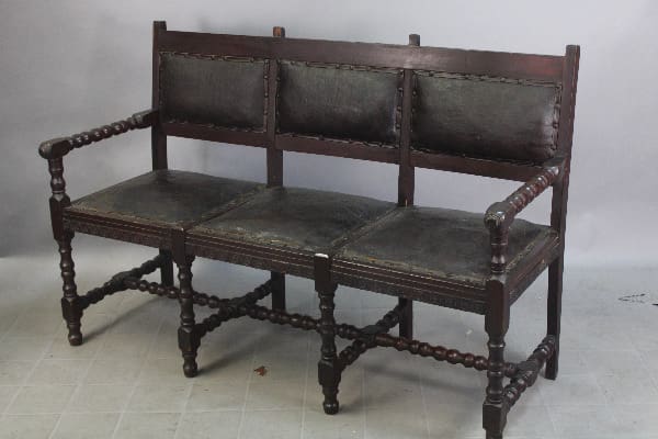 Antique wooden bench with black leather upholstery.