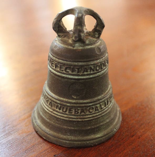 Bronze bell with engraved text on wood.