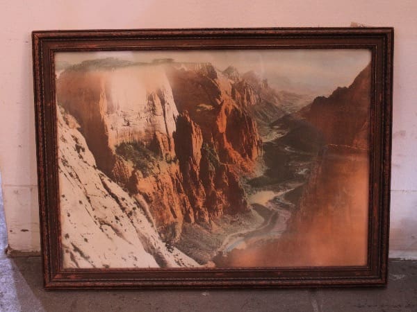 Framed landscape painting of a canyon scene.