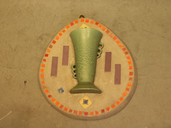 Green vase on decorative circular wall plaque.