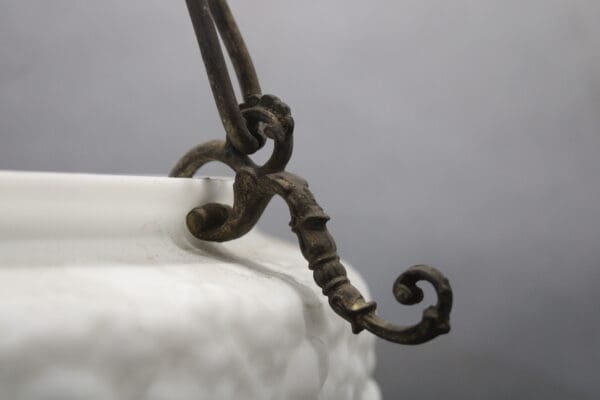 Ornate metal hook on white ceramic dish.