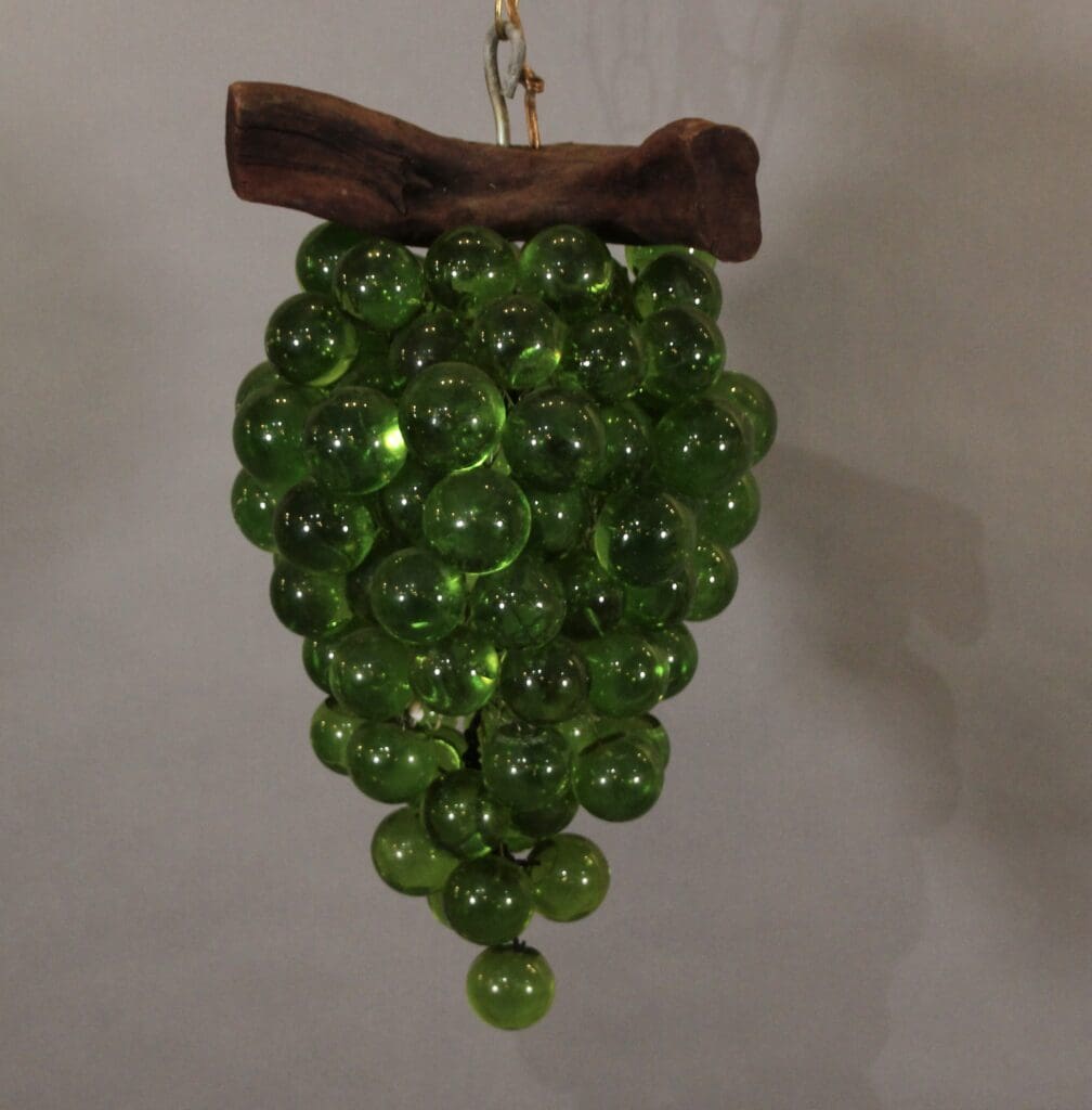 Green glass grapes hanging from wooden branch.