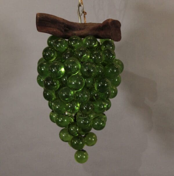 Green glass grapes hanging from wooden branch.